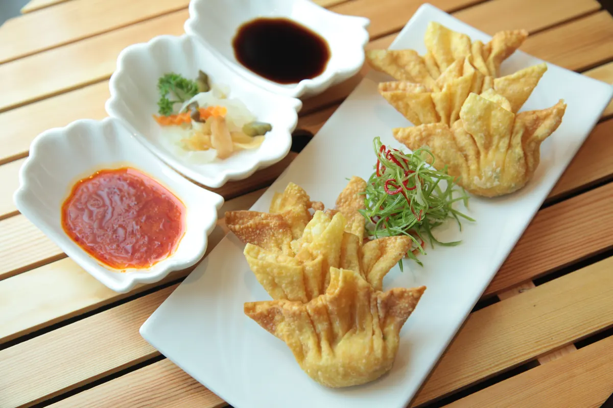 Crab rangoon served on a white plate with dipping sauces