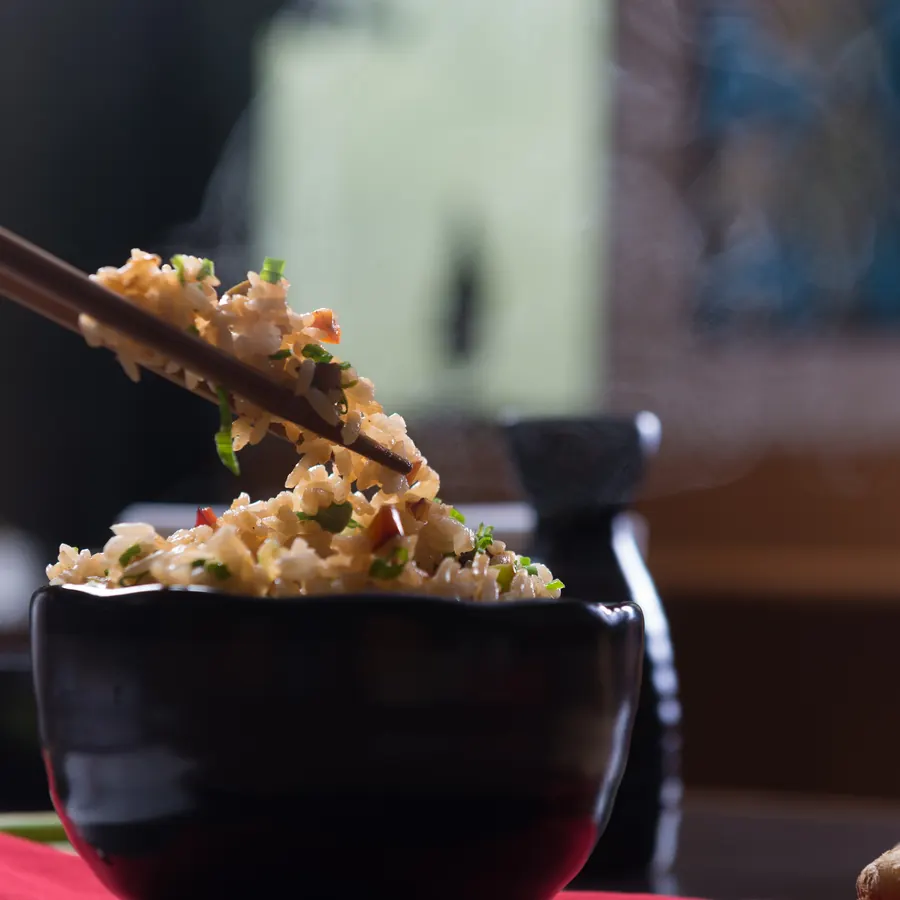 Chopsticks lifting fried rice from a black bowl